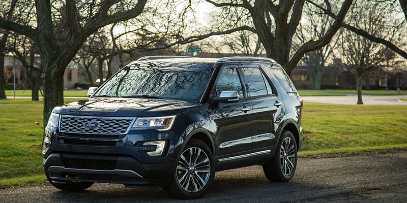 Image shows a blue Ford Explorer parked on a street with trees in the background.