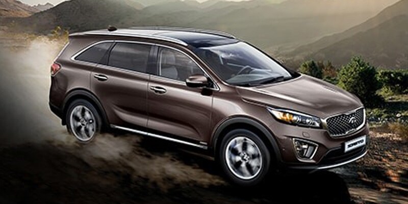 Image shows a brown Kia Sorento driving down a dusty mountain road.