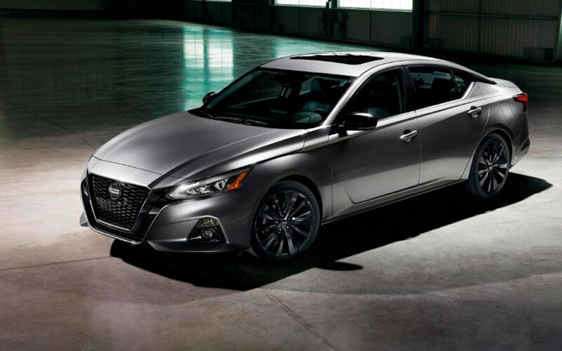 Image shows a silver Nissan Altima parked on concrete inside a building with dramatic shadows.