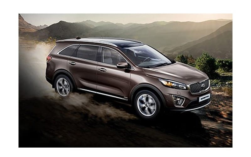 Image shows a brown Kia Sorento driving down a dusty mountain road.