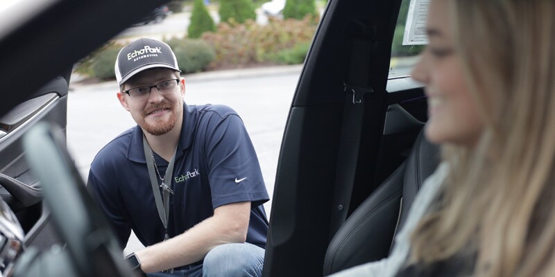 Image shows an EchoPark Experience Guide talking with a guest who’s in the driver’s seat of a car.
