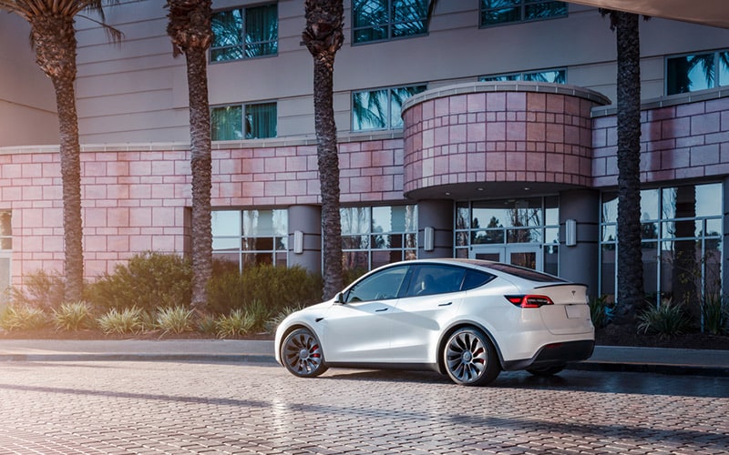 A white Tesla Model Y is parked on a street made of brick pavers, in front of an office building. 