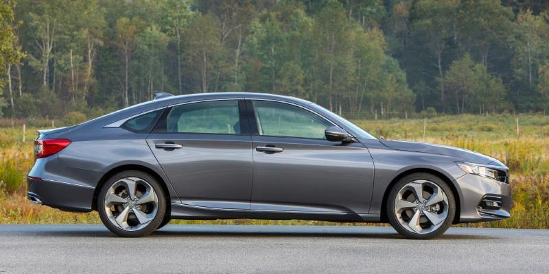 Image shows gray Honda Accord parked on pavement, with trees and mountains in the background.