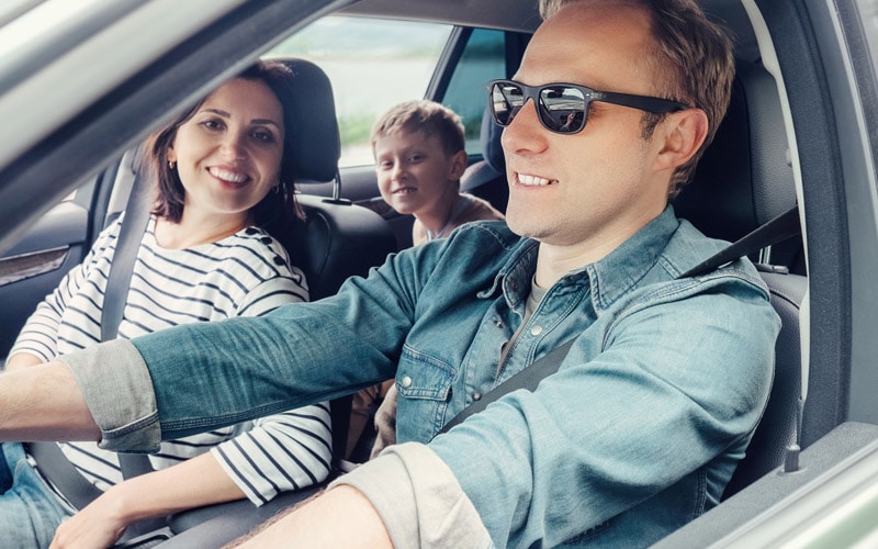 Image shows a man and woman in the front seats of a car, with a boy in the backseat.