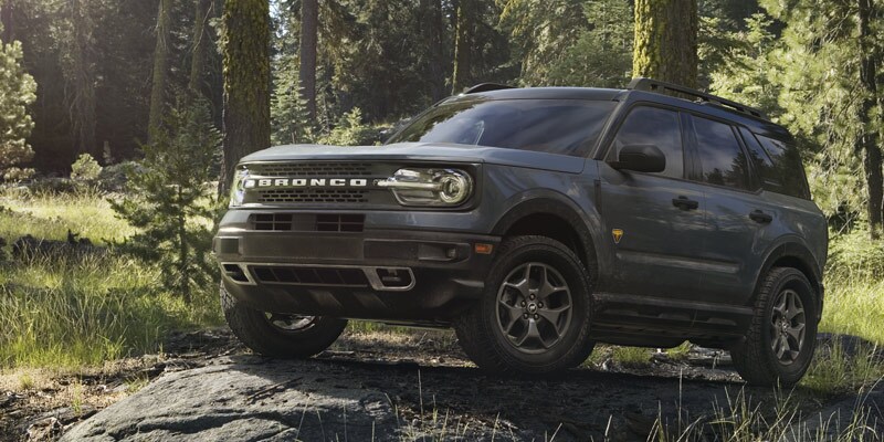 Photo shows a dark gray Ford Bronco Sport parked on a small rocky incline in a wooded area.