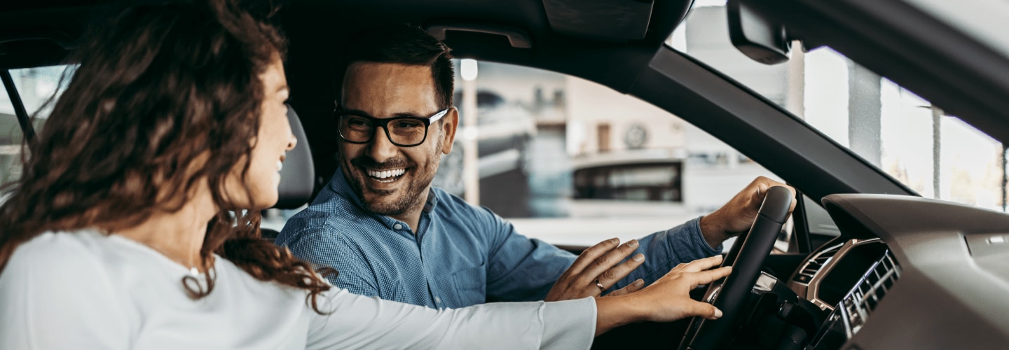 Male and female smiling and jovial in the interior of a car.