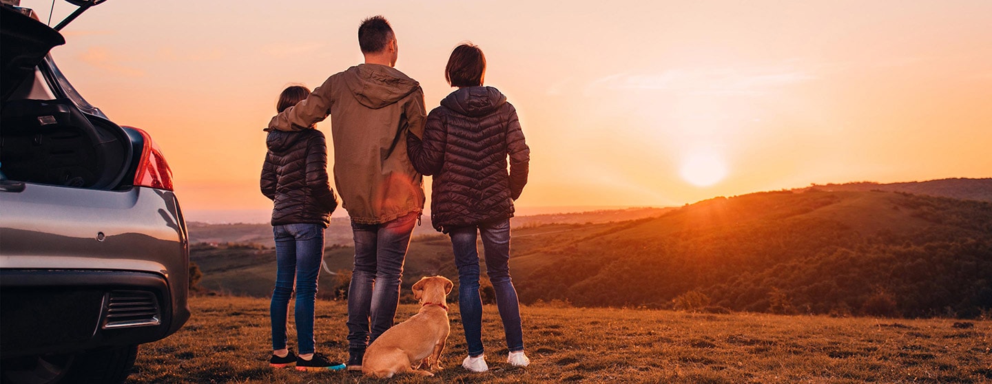 Family watching the sunset next to their car with hatch open